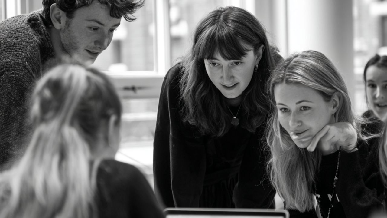 A small group leaning in together to look at a laptop screen.